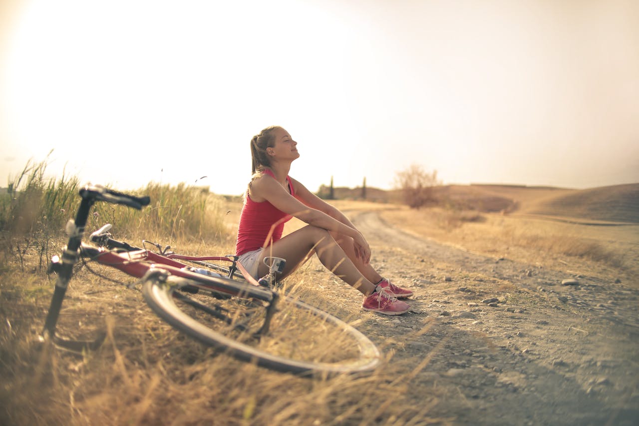 home-hero-2 Full body of female in shorts and top sitting on roadside in rural field with bicycle near and enjoying fresh air with eyes closed