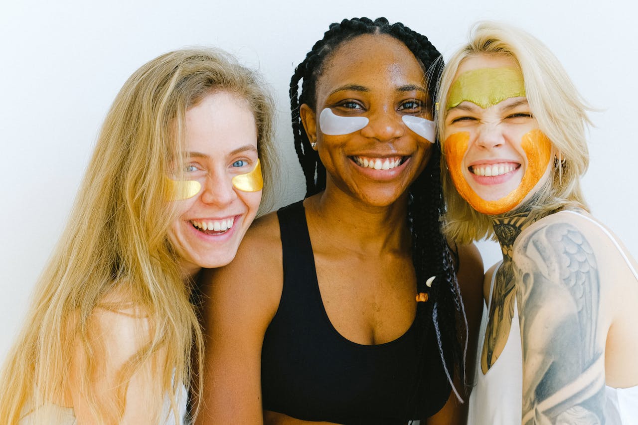 services-02 Group of women with masks and patches smiling while looking at camera and laughing during skincare procedure in studio on weekend