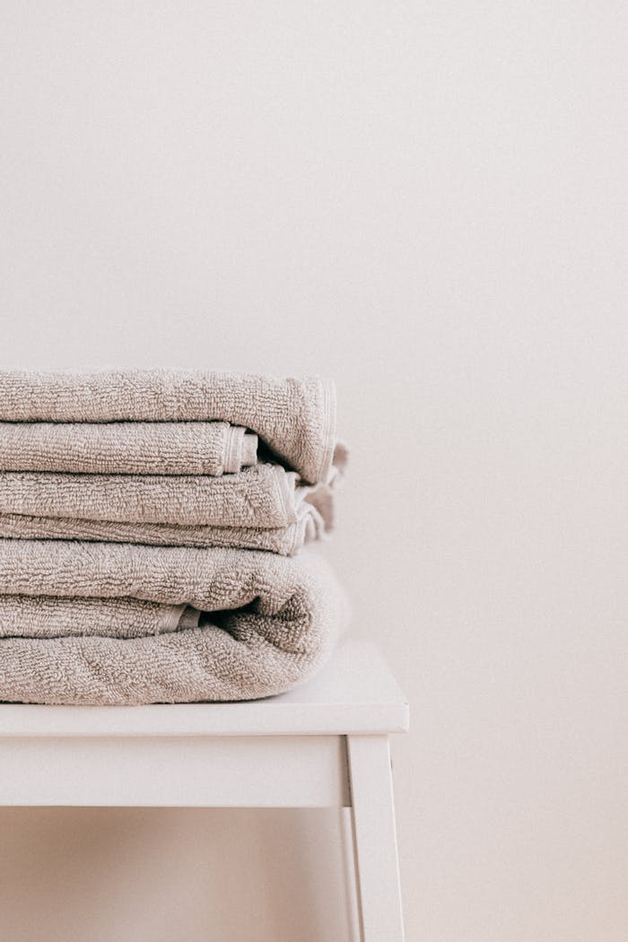about-us-01 Stack of soft clean fresh gray towels placed on white minimalist stool against beige wall