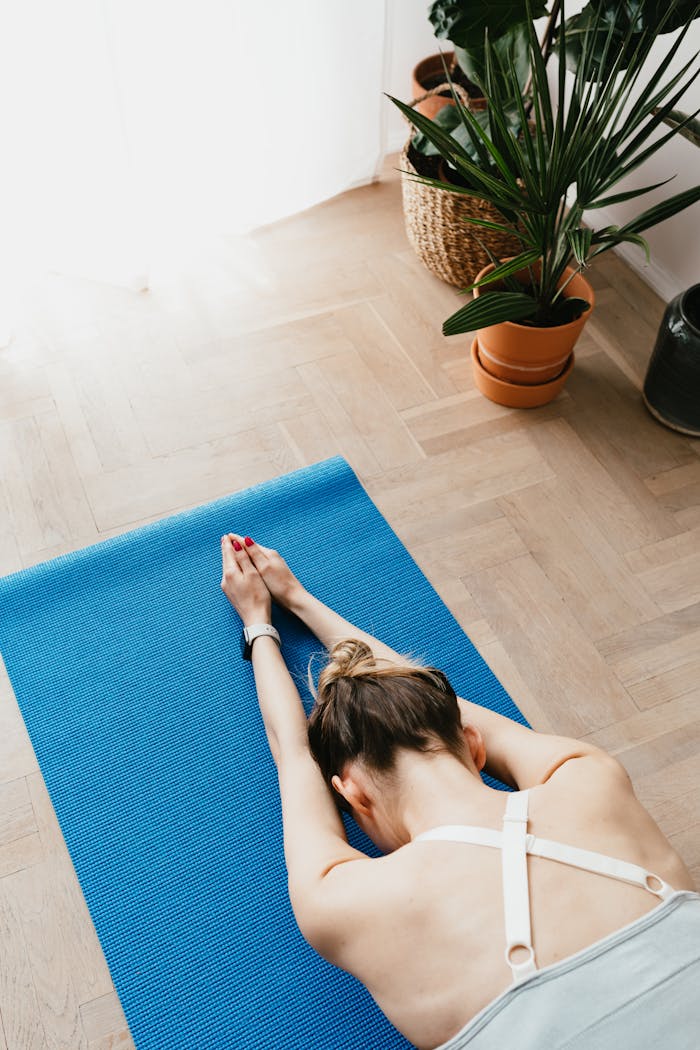 services-03 Top view of fit faceless lady in sports clothes lying on blue yoga mat in Child pose at home near potted plants